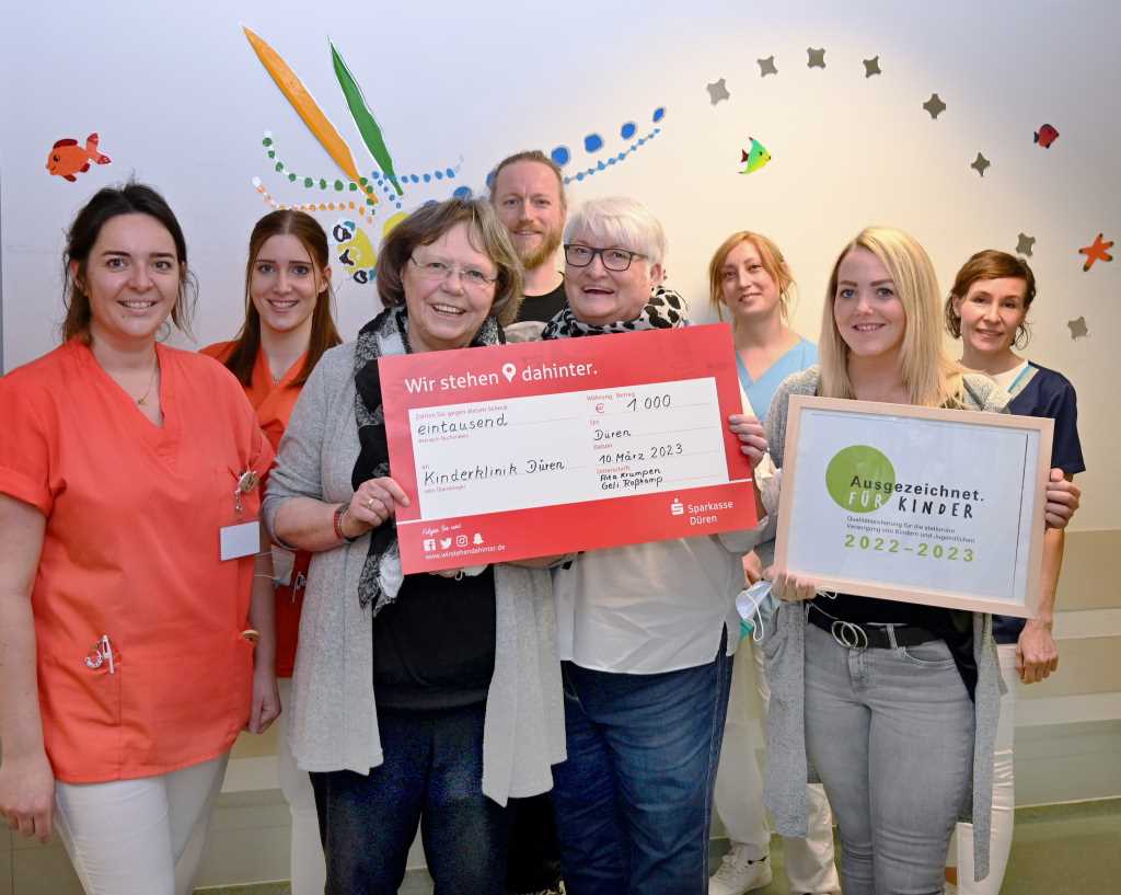 Foto (© Tatjana Opgenorth): Freuen sich, dass die kleinen Patienten der Kinderklinik dank der Spende der Dürener Schatztruhe neue Spielgeräte für die umgebauten Stationen K2 und K3 bekommen werden: Die beiden Vorsitzenden des gemeinnützigen Vereins, Rita Krumpen (rechts im Bild mit Scheck) und Geli Roßkamp, im Kreis von Kinderfachpflegekräften und Alexander Bey, Leitender Oberarzt am St. Marien-Hospital Düren.