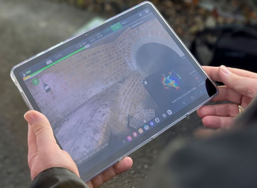 Bürgermeister Frank Peter Ullrich (r.) und der Leiter der Stadtentwässerung Düren, Benjamin Savelsberg, verfolgen den Drohnenflug durch den Kanal auf einem Tablet in Echtzeit.